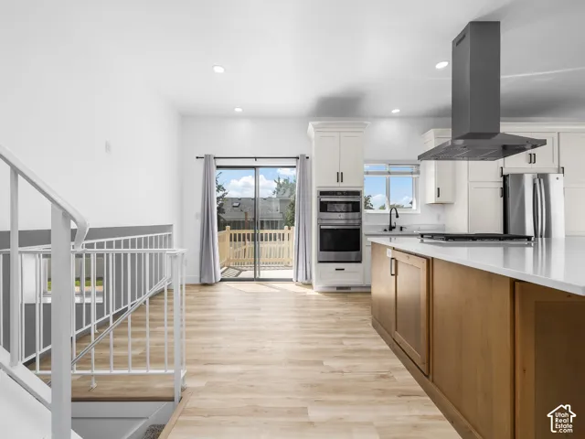 Open-concept kitchen and living area featuring white cabinetry, stainless steel appliances, a black range hood, and wood-finish flooring throughout