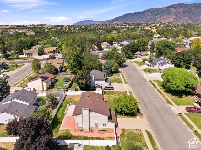 Aerial view showcasing a residential property nestled within a tree-lined neighborhood, featuring a brown-roofed residence with established landscaping, manicured lawn, and mature trees throughout the surrounding streetscape