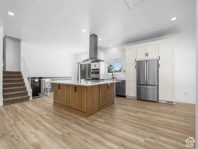 Wood-finish flooring, recessed lighting, white cabinetry, stainless steel appliances, and a central island with a light-toned countertop