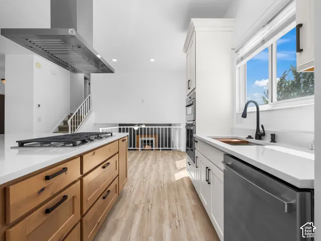 Modern galley kitchen featuring natural wood cabinetry with integrated hardware, stainless steel range hood, quartz countertops, and a black matte faucet