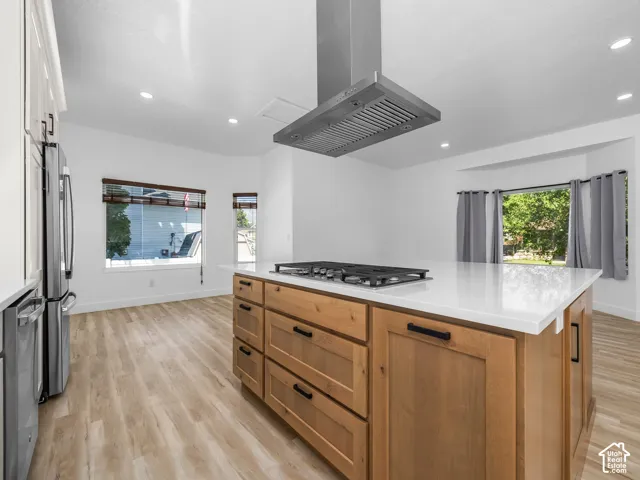 Central kitchen island with a built-in gas cooktop, sleek stainless steel range hood, and light-toned wood-finish flooring