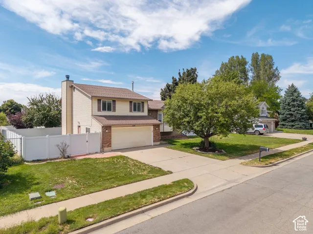 Two-story residence with a two-car garage, featuring a white privacy fence and a mature shade tree