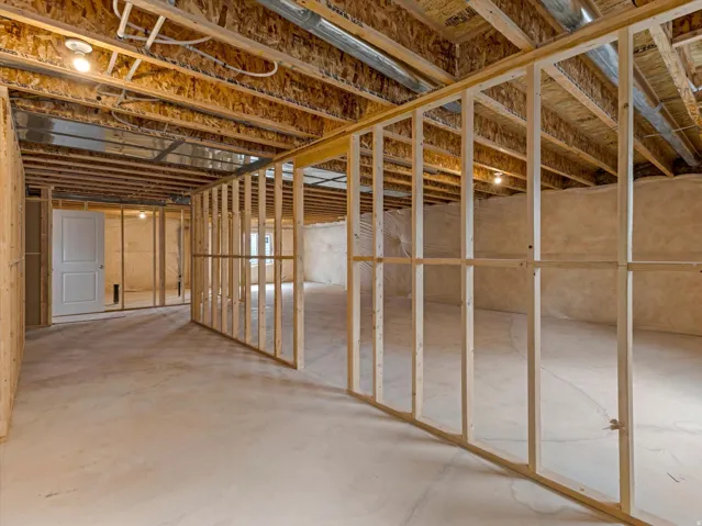 Unfinished basement with exposed wood framing, concrete flooring, and an existing interior door