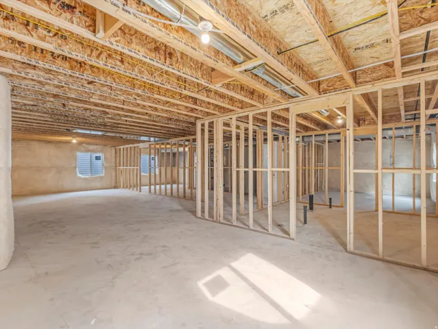 Unfinished basement with exposed ceiling joists, wood framing, concrete flooring, and windows with horizontal blinds