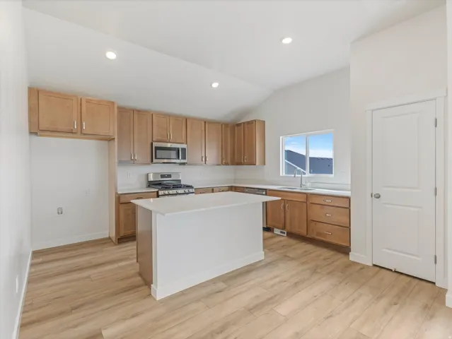 Kitchen featuring a central island, light wood-finish cabinetry, stainless steel appliances, and wood-finish flooring