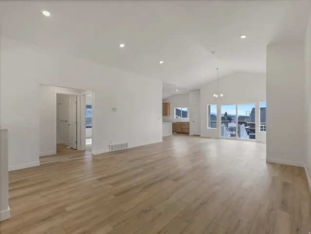 Spacious living area featuring wood-finish flooring, vaulted ceilings, recessed lighting, and expansive glass sliding doors