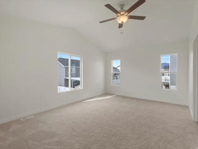 Vaulted ceiling featuring a ceiling fan with integrated lighting, multiple windows, and neutral carpeting