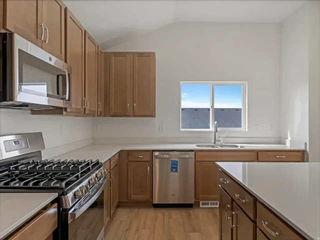 Chef's kitchen featuring warm wood cabinetry, stainless steel appliances including a professional-style gas range and dishwasher, quartz countertops, and a spacious island with seating