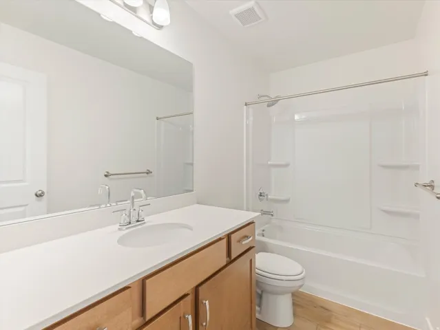 Vanity with a white countertop and undermount sink, wood-finish cabinetry with silver hardware, full-width mirror, and a shower-tub combination with a white surround
