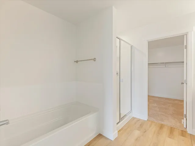Soaking tub, glass-enclosed shower, wood-finish flooring, and a walk-in closet with carpeted flooring and built-in shelving