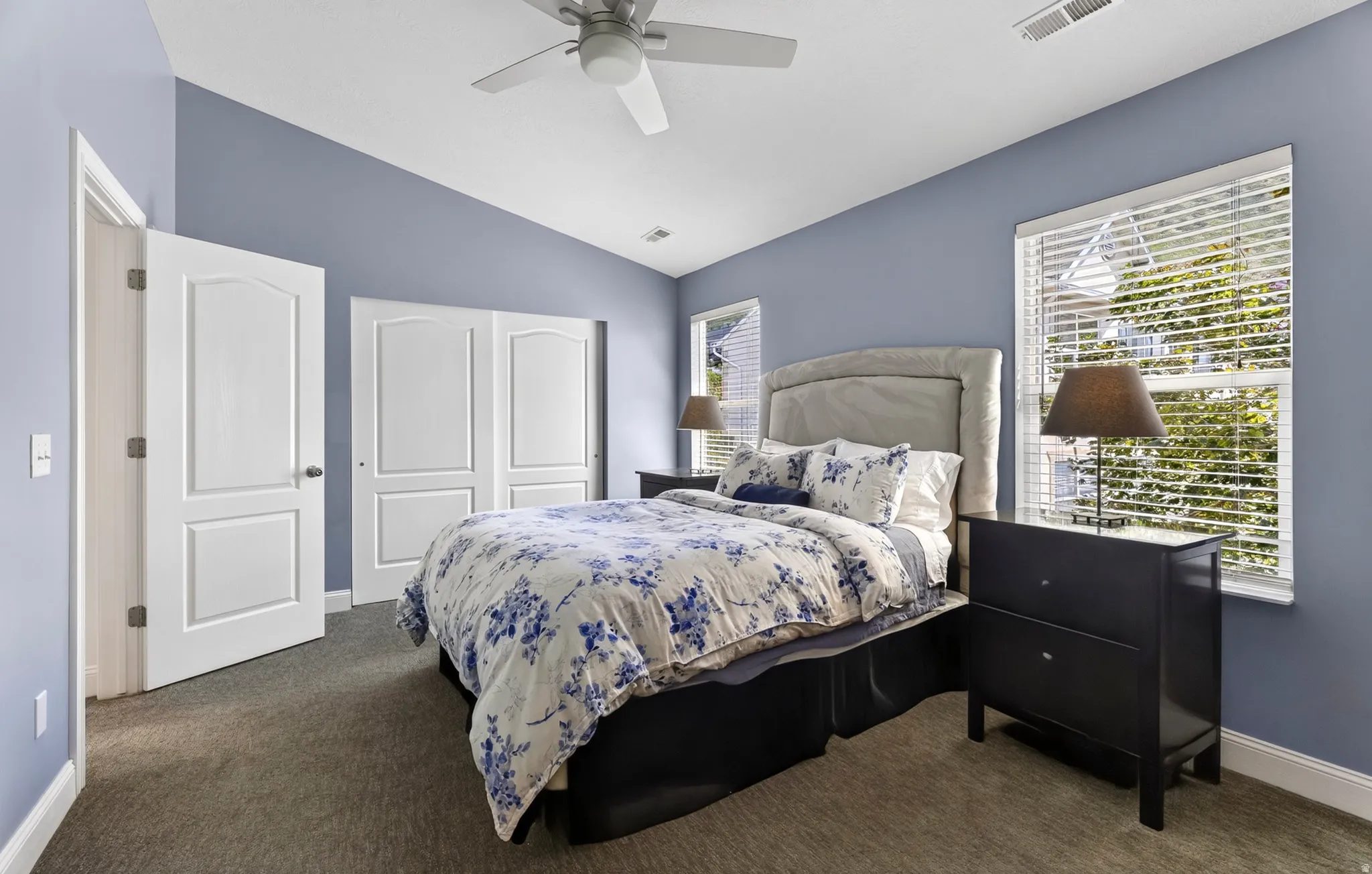 Vaulted ceiling featuring a ceiling fan, dual white panel doors, and two windows with blinds