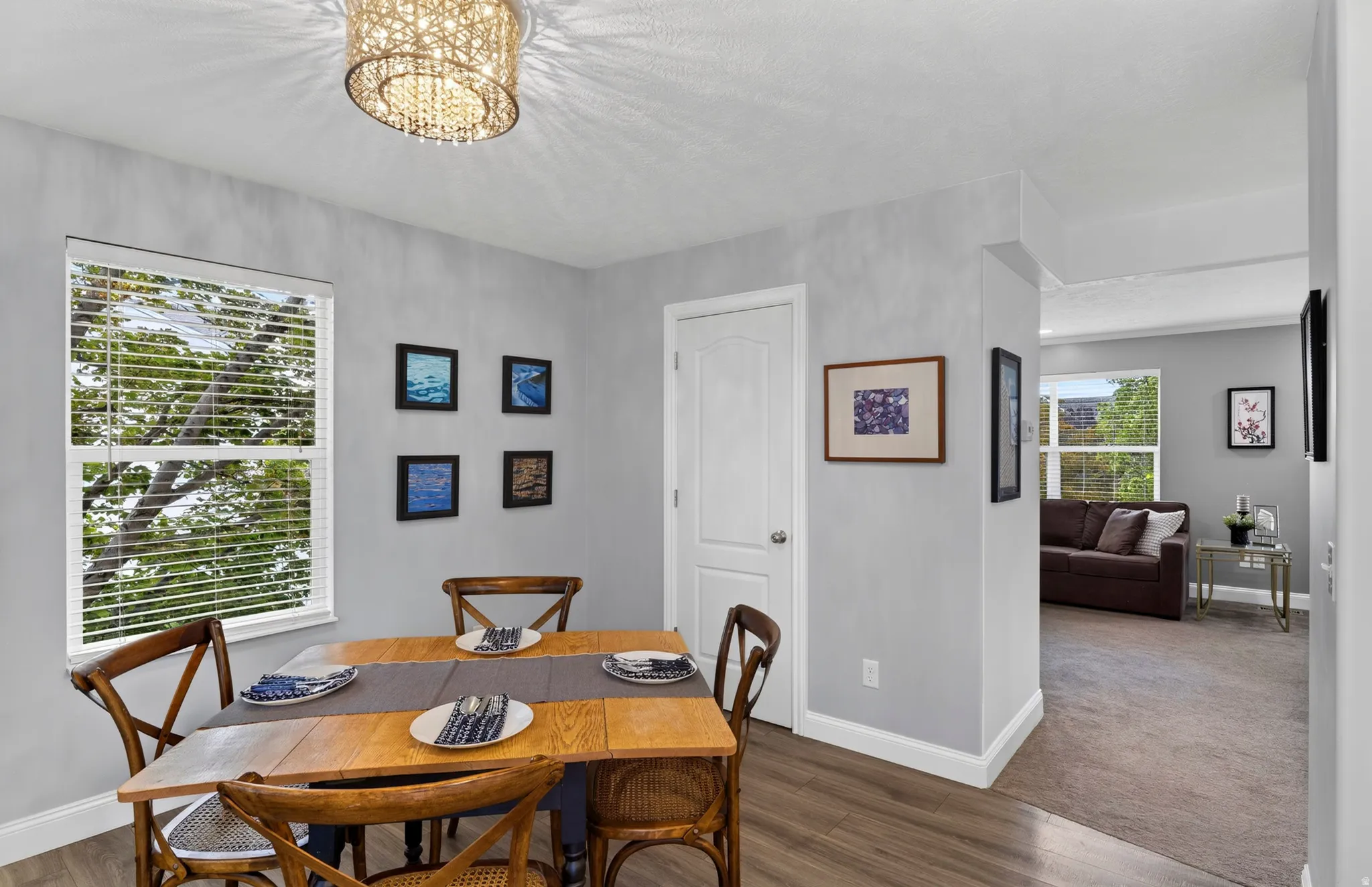 Bright dining area featuring a round wood-finish table, hardwood flooring, and large windows with plantation shutters