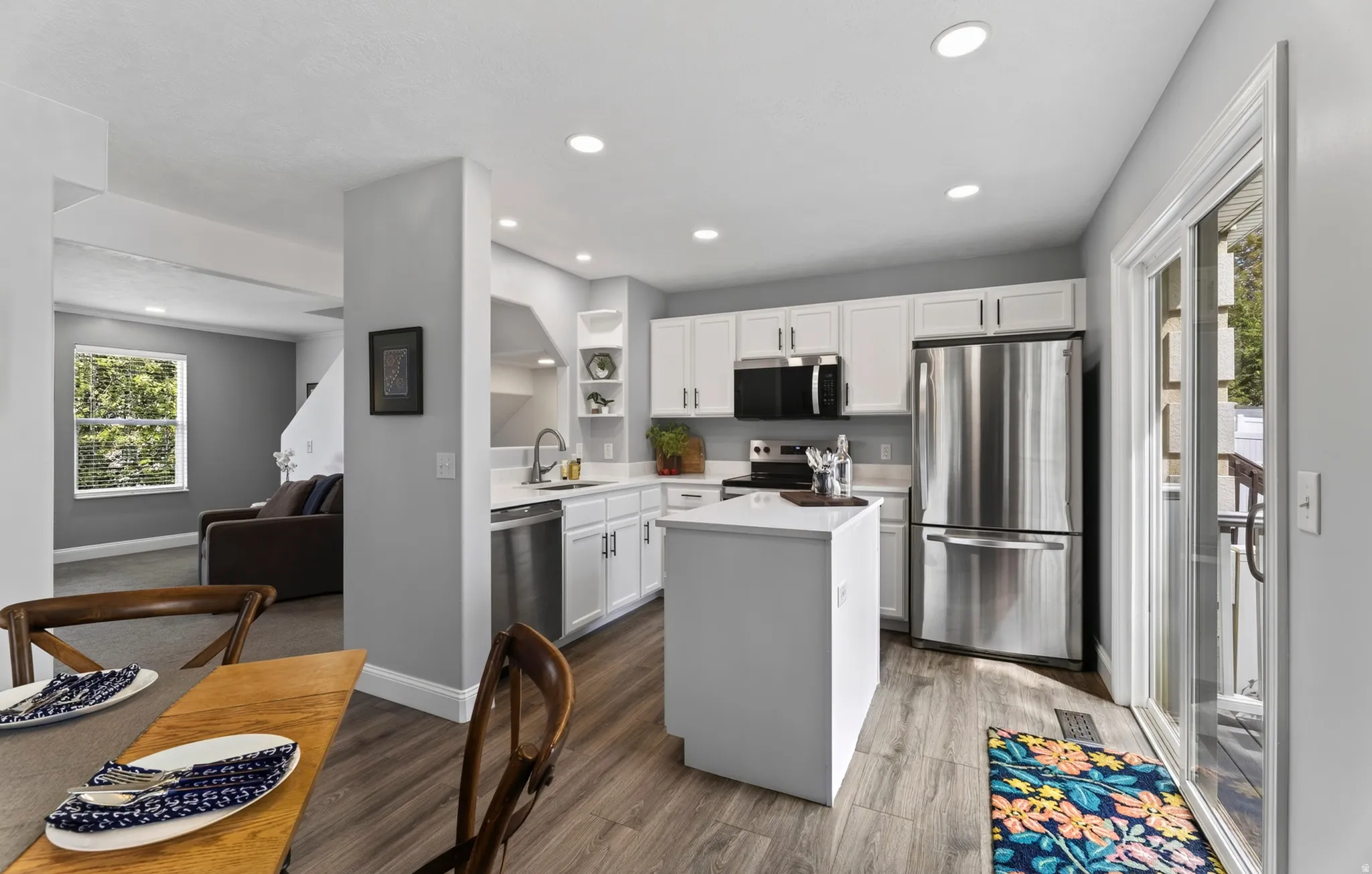 Kitchen featuring wood-finish flooring, white cabinetry, a center island, stainless steel appliances, and a sliding glass door