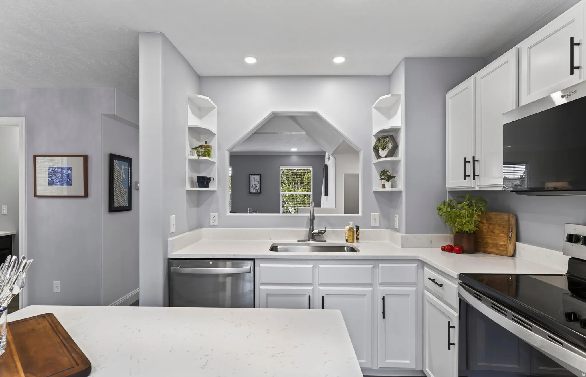White cabinetry with matte black hardware, stainless steel appliances, light-toned countertops, recessed lighting, and a kitchen pass-through