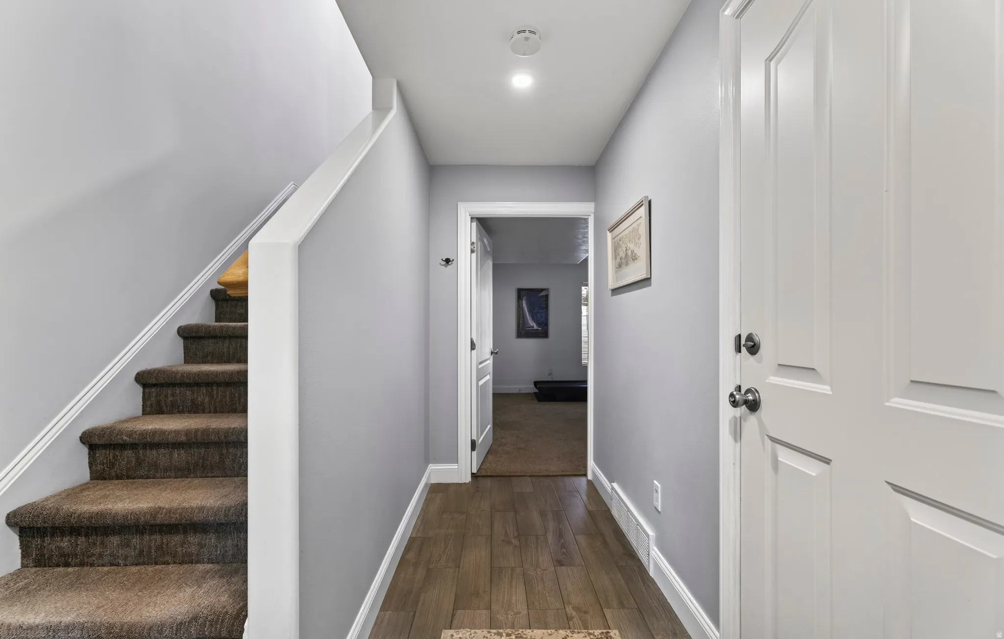 Wood-finish flooring, staircase with carpeted treads, white trim, recessed lighting, and a paneled interior door