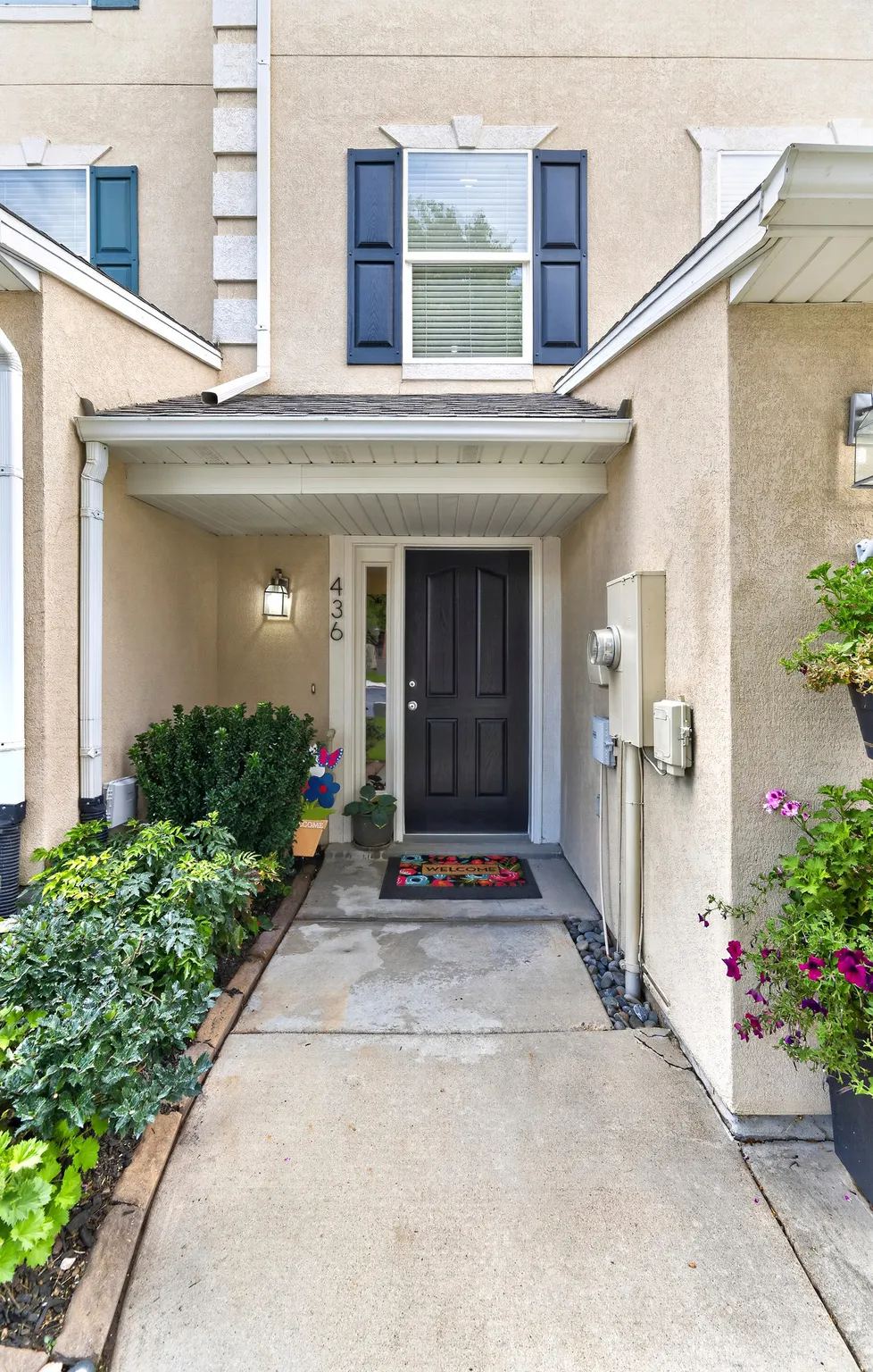 Stucco exterior with a covered entry, dark paneled entry door, and dark shutters