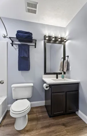 Wood-finish flooring, dark wood vanity with white countertop, black-framed mirror, and a modern light fixture