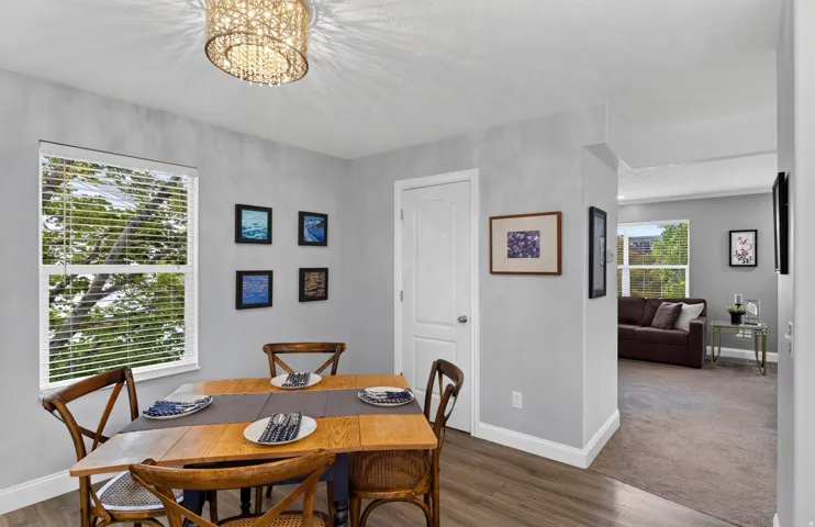 Bright dining area featuring a round wood-finish table, hardwood flooring, and large windows with plantation shutters