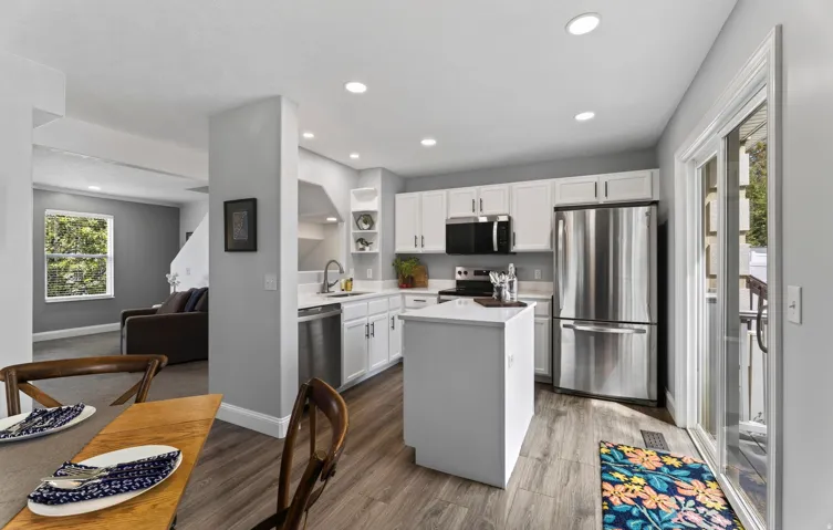 Kitchen featuring wood-finish flooring, white cabinetry, a center island, stainless steel appliances, and a sliding glass door
