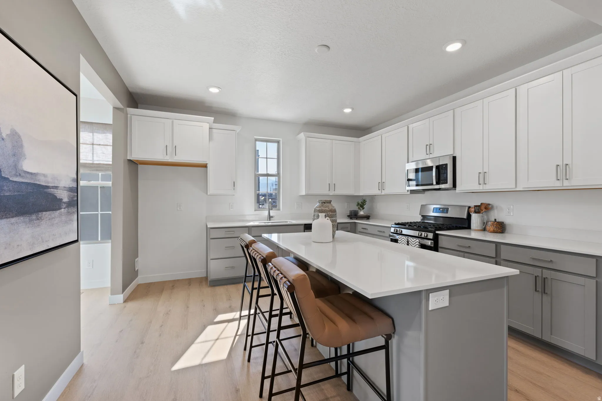 Contemporary kitchen featuring two-tone cabinetry, a central island with countertop seating, stainless steel appliances, and light wood-finish flooring