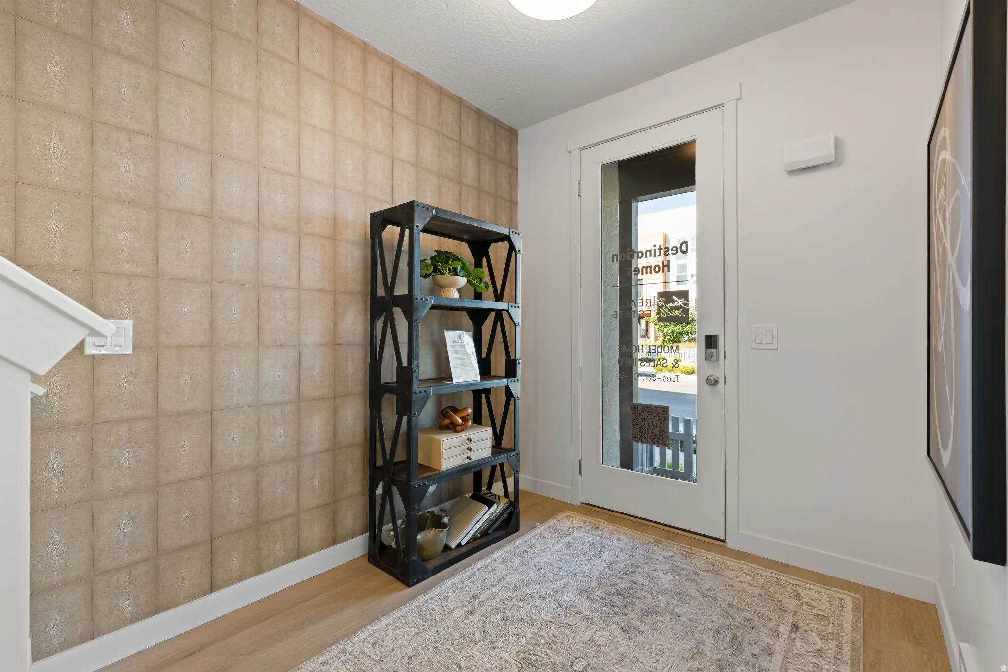 Wood-finish flooring, patterned accent wall, modern glass-paneled door, recessed lighting, and white trim