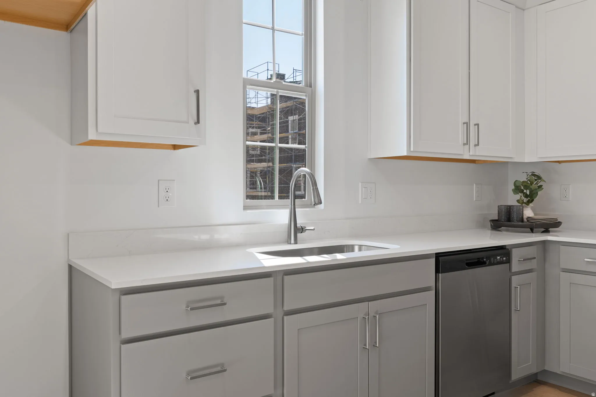 Kitchen featuring white upper cabinetry, gray lower cabinetry, light-toned countertops, a stainless steel sink with a pull-down faucet, and a stainless steel dishwasher