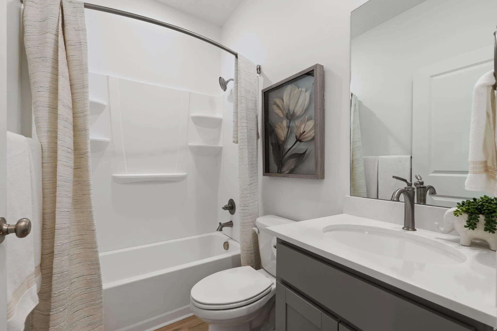 Bathroom featuring a white tub/shower combination, a gray vanity with a white countertop and integrated sink, a frameless mirror, and wood-finish flooring
