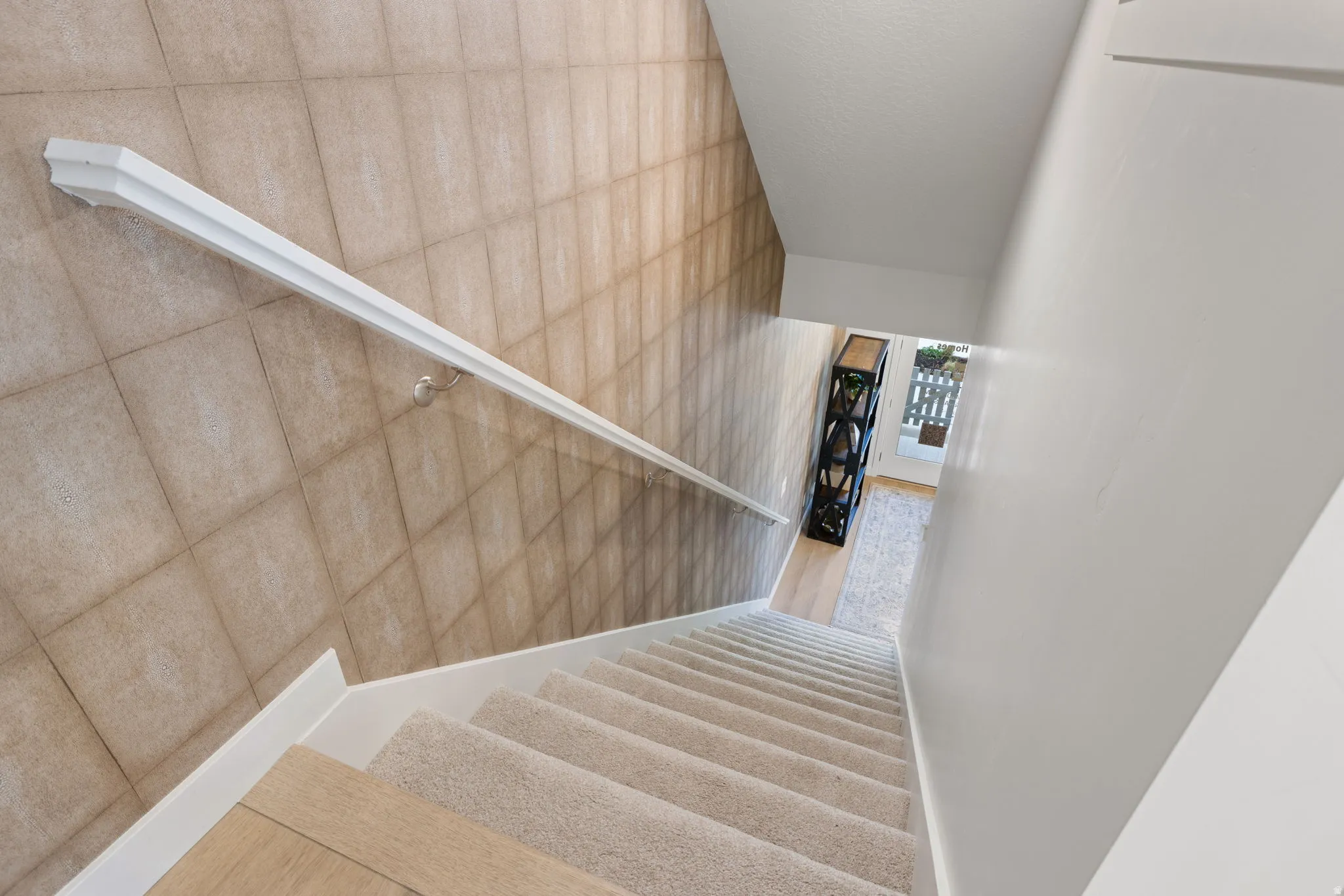 Stairwell featuring carpeted treads, wood-finish risers, and a white handrail set against a tiled wall