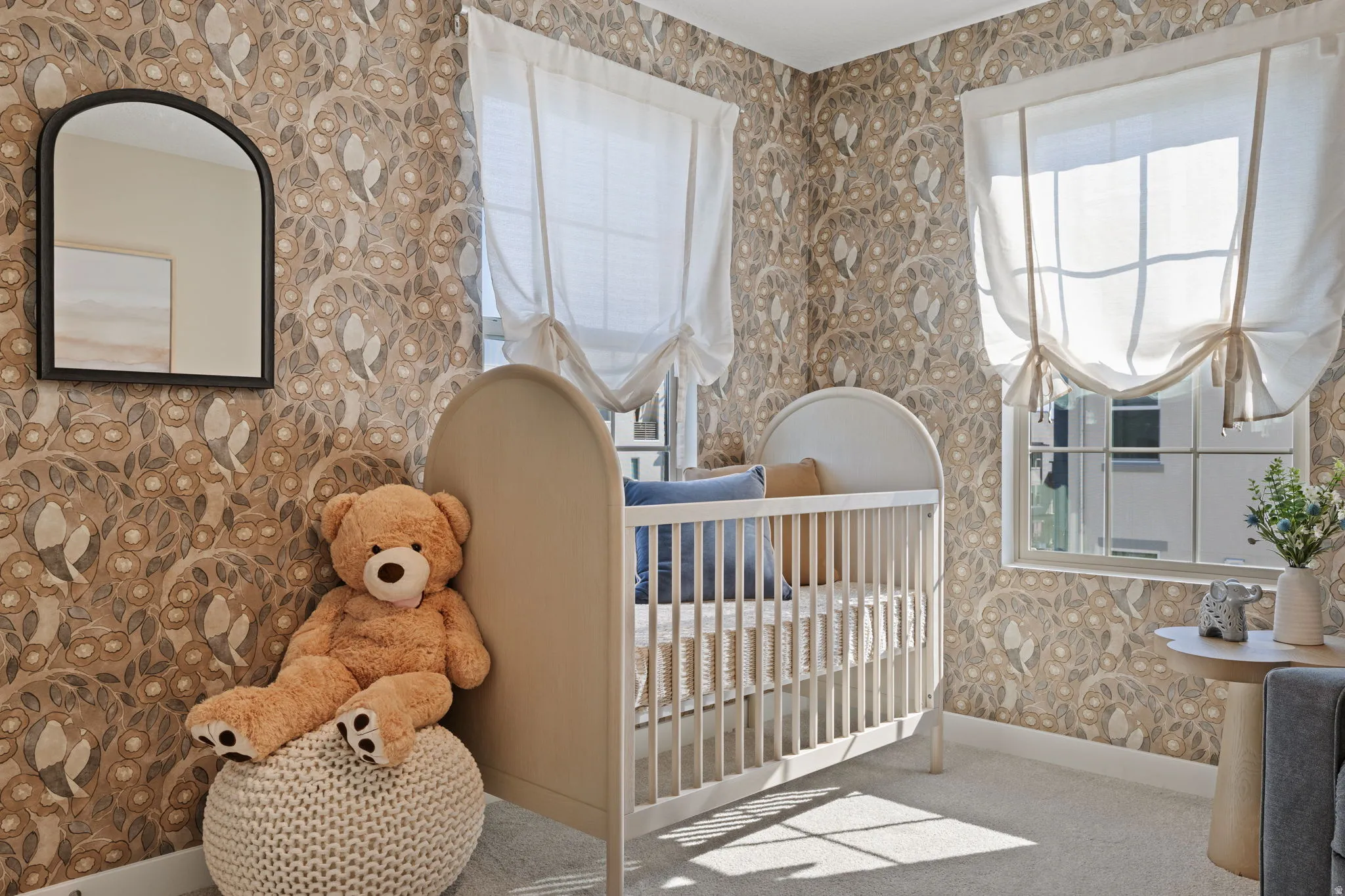 Patterned wallpaper with an arched mirror, two windows with Roman shades, and carpeting