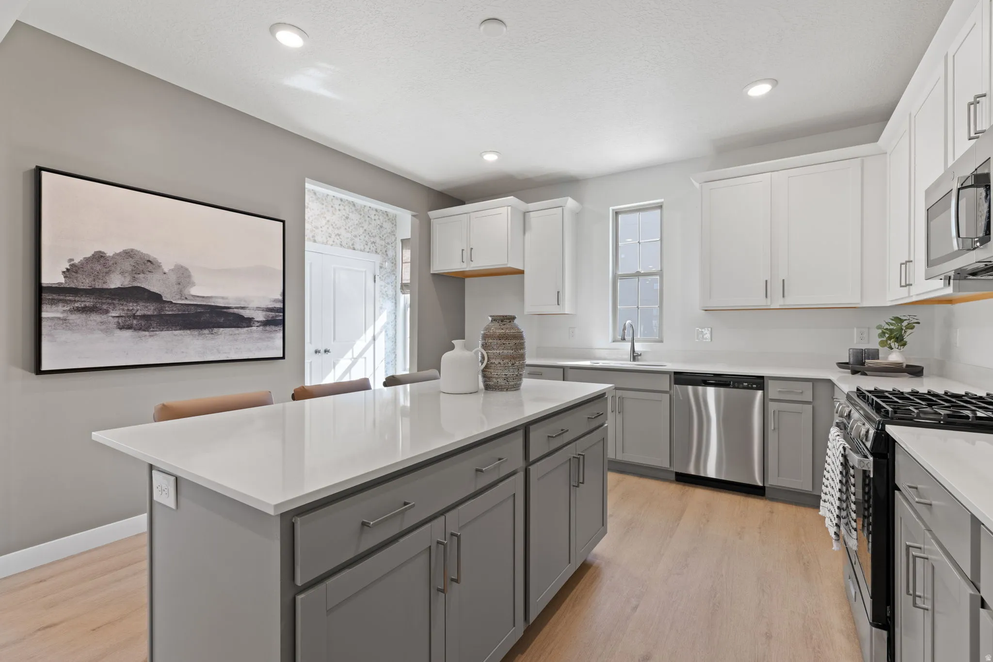 Kitchen featuring an island with a light-toned countertop, two-tone cabinetry, stainless steel appliances, wood-finish flooring, and recessed lighting