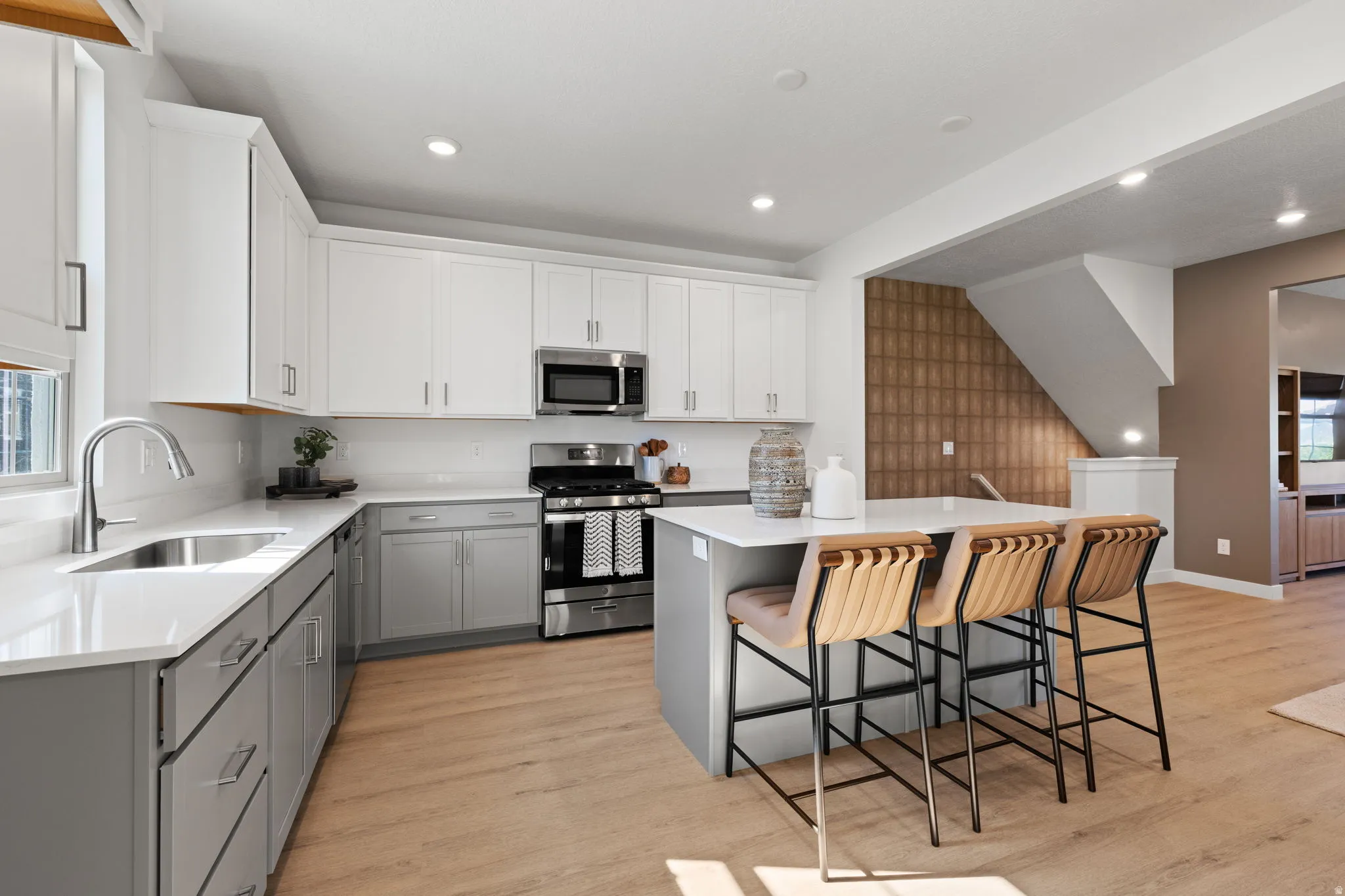 Kitchen with two-tone cabinetry, stainless steel appliances, a center island with counter seating, and wood-finish flooring