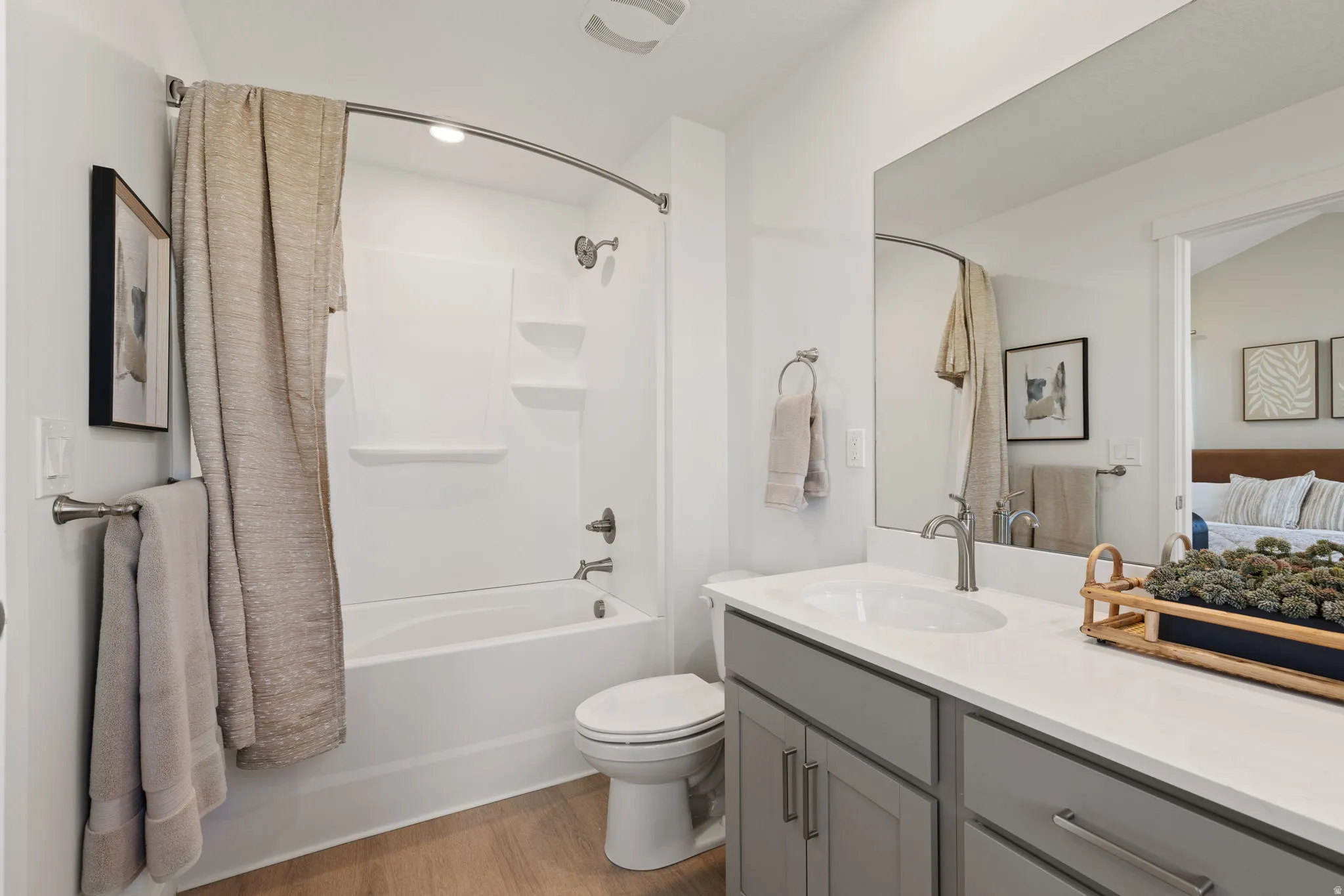 Bathroom featuring a white tub/shower combination, light wood-finish flooring, a vanity with a white countertop, and a large wall mirror