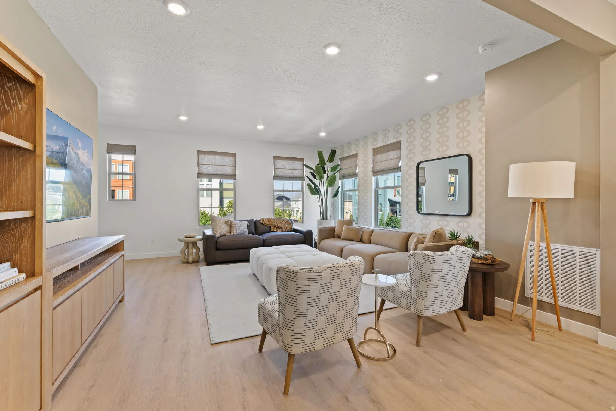 Recessed ceiling lighting, wood-finish flooring, built-in media console, multiple windows with blinds, and decorative wall paneling
