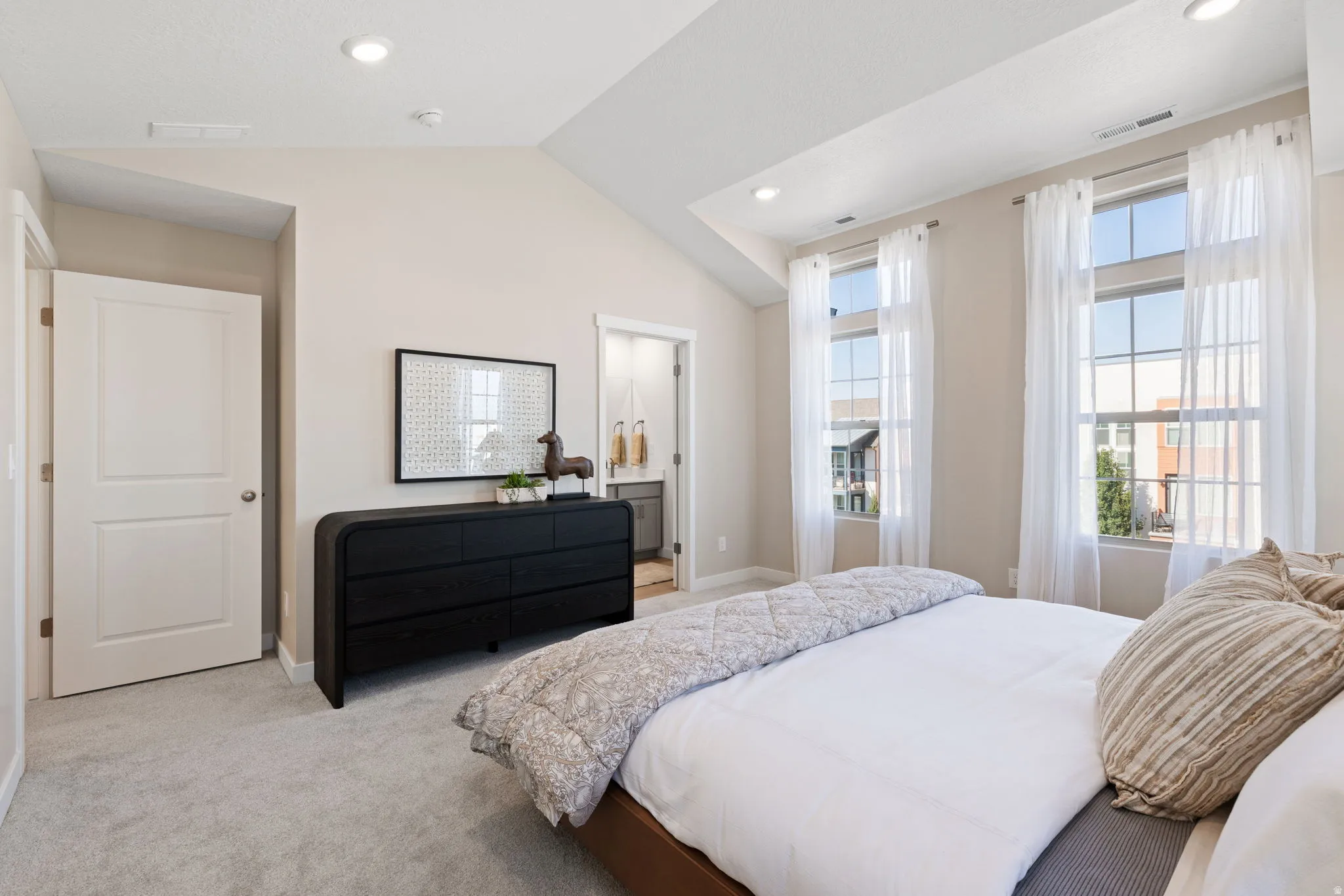 Vaulted ceiling, recessed lighting, two large windows, light-colored carpeting, and a white paneled door