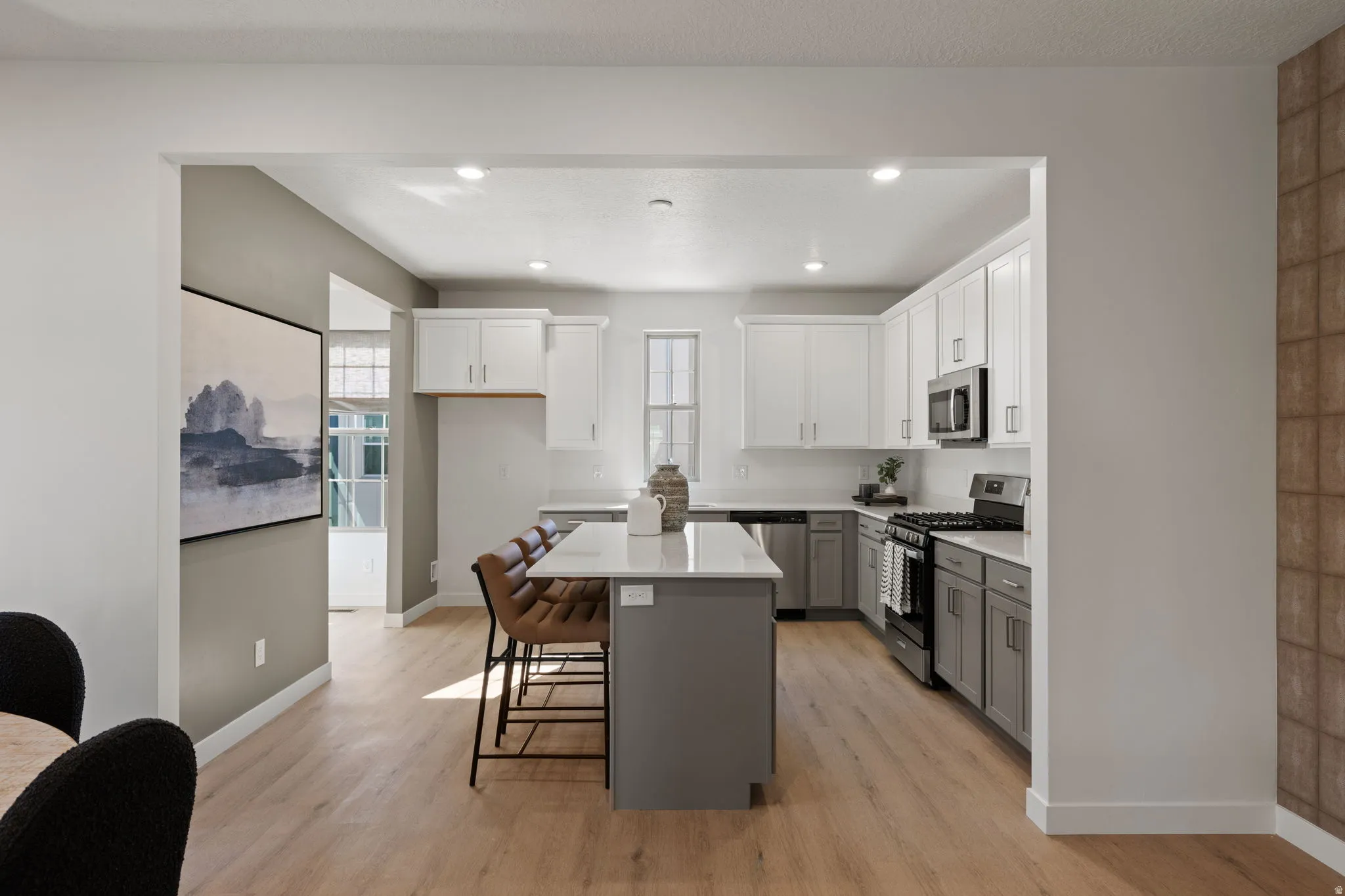Kitchen featuring a central island with a breakfast bar, stainless steel appliances, wood-finish flooring, two-tone cabinetry, and recessed lighting