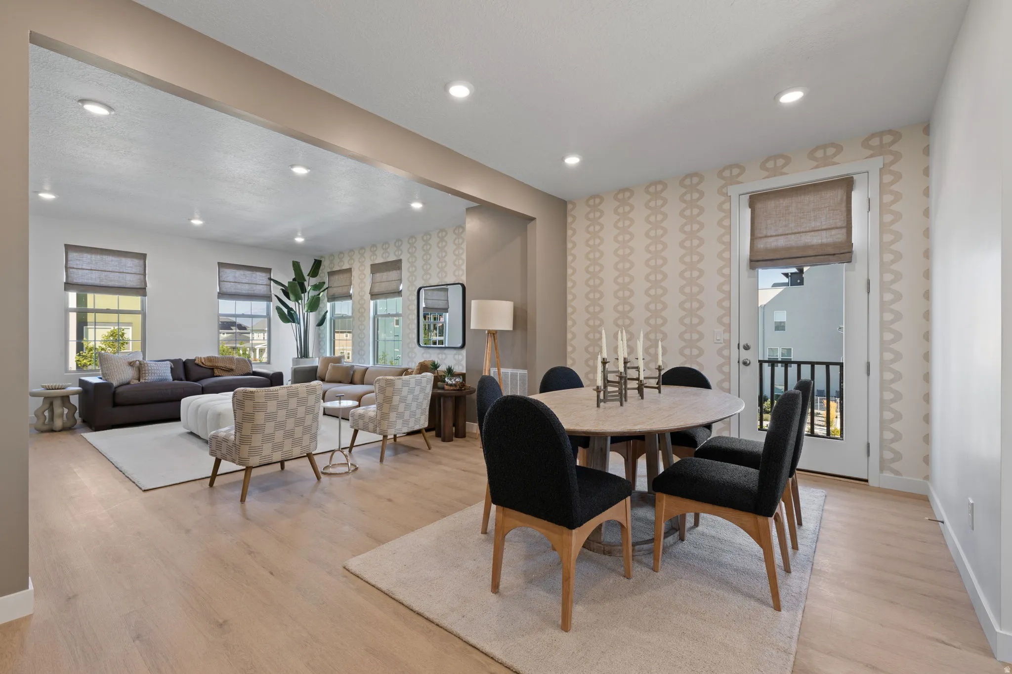 Open-concept living and dining area featuring light wood-finish flooring, recessed ceiling lighting, and large windows with cellular shades