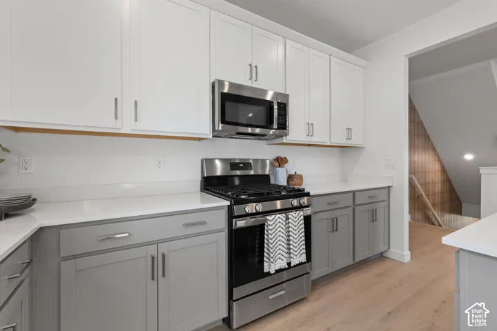 Two-tone cabinetry with white upper and gray lower cabinets, stainless steel appliances, white countertops, wood-finish flooring, and a built-in microwave