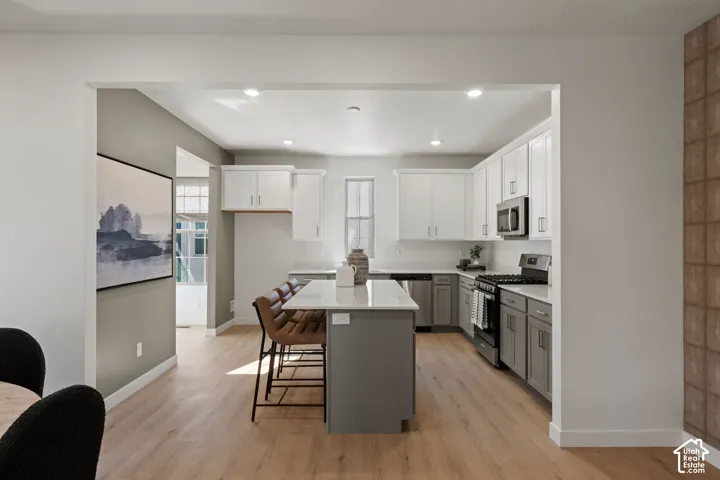 Kitchen featuring a central island with a breakfast bar, stainless steel appliances, wood-finish flooring, two-tone cabinetry, and recessed lighting