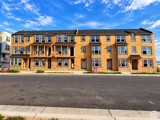 Newly constructed multi-level townhome building featuring multiple windows, distinct bay window sections, and individual entryways with protective overhangs