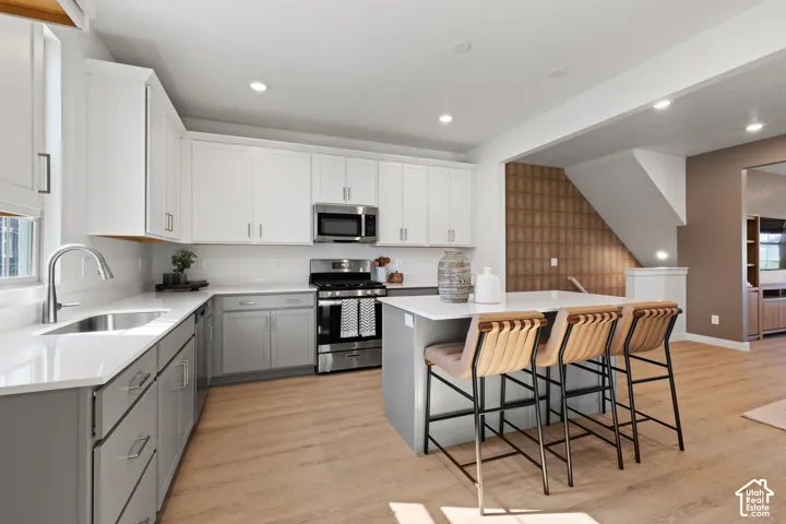 Kitchen with two-tone cabinetry, stainless steel appliances, a center island with counter seating, and wood-finish flooring