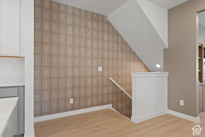 Wood-finish flooring, staircase with white railing, patterned accent wall, white wall cabinetry, and light countertop