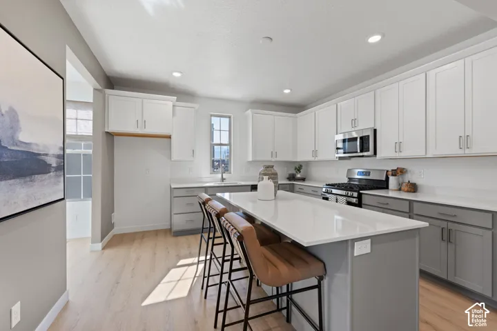 Contemporary kitchen featuring two-tone cabinetry, a central island with countertop seating, stainless steel appliances, and light wood-finish flooring