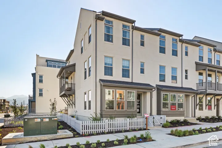 Multi-story stucco exterior with multiple windows, individual balconies, and a white picket fence