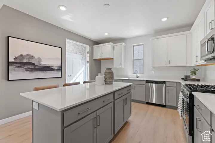 Kitchen featuring an island with a light-toned countertop, two-tone cabinetry, stainless steel appliances, wood-finish flooring, and recessed lighting