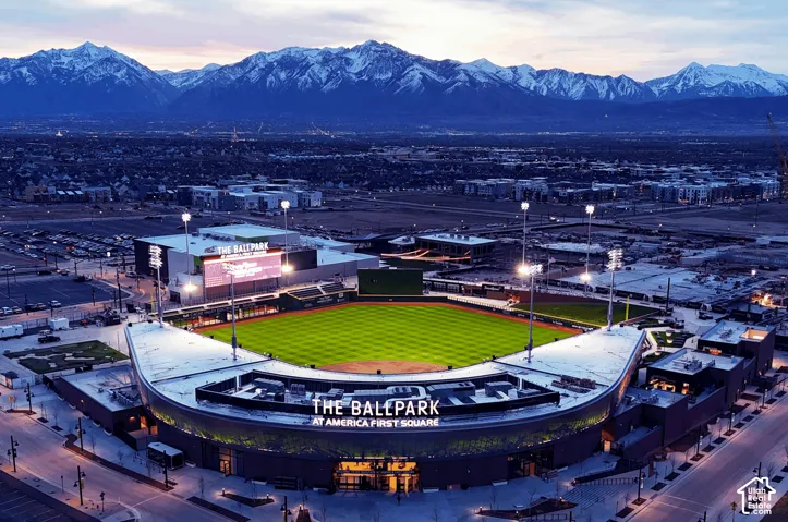 Aerial perspective featuring a stadium with a vibrant green field, surrounded by urban structures and a distant mountain range