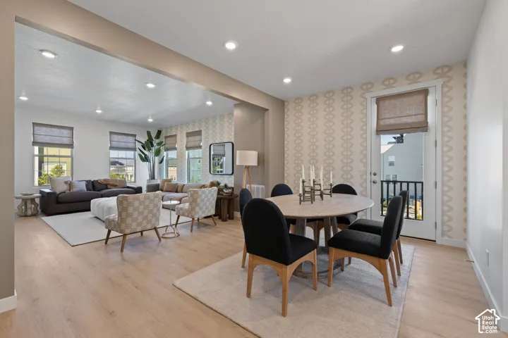 Open-concept living and dining area featuring light wood-finish flooring, recessed ceiling lighting, and large windows with cellular shades
