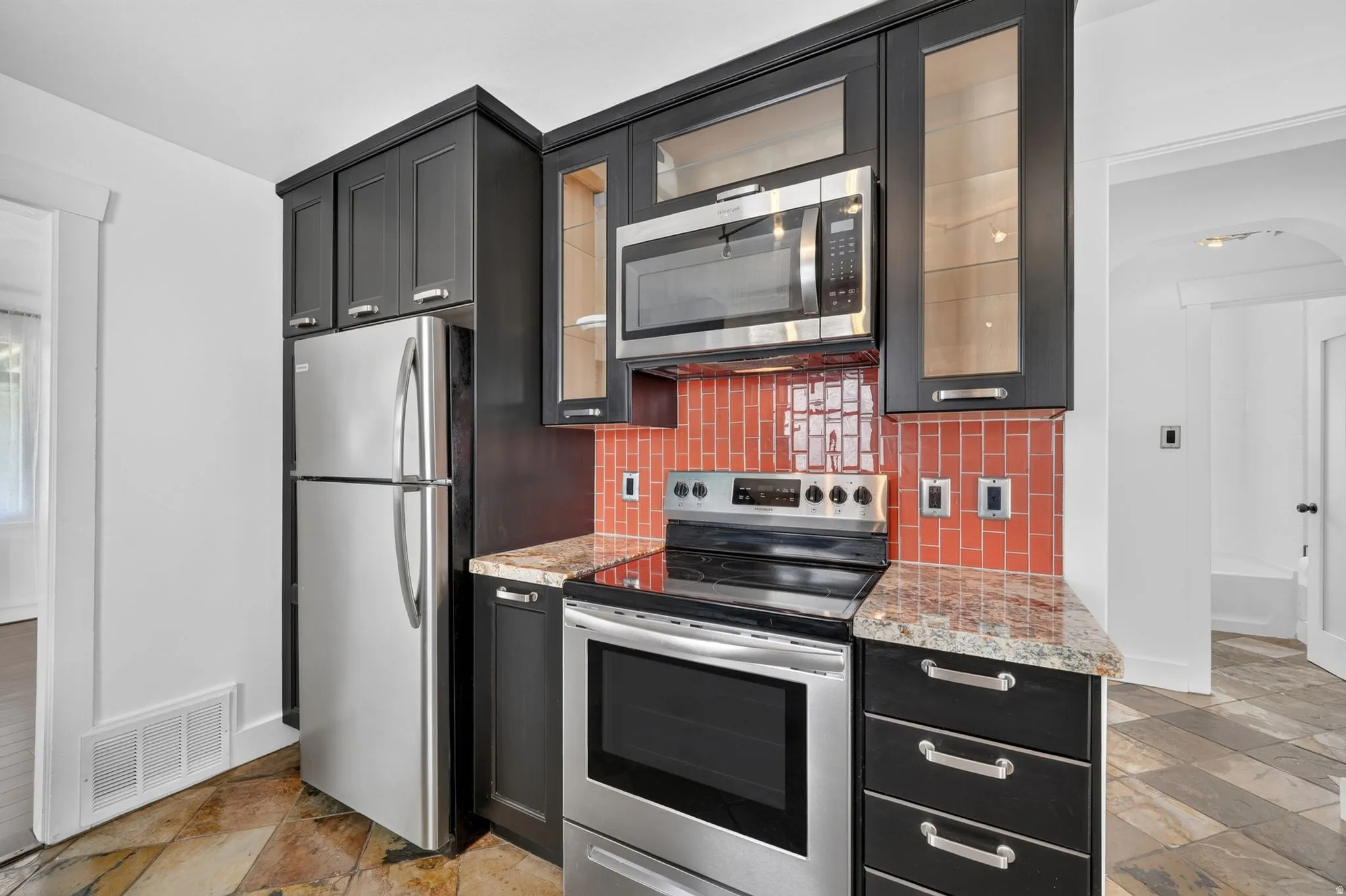 Kitchen featuring stainless steel appliances, dark wood-finish cabinetry, granite-style countertops, and a vibrant red tile backsplash