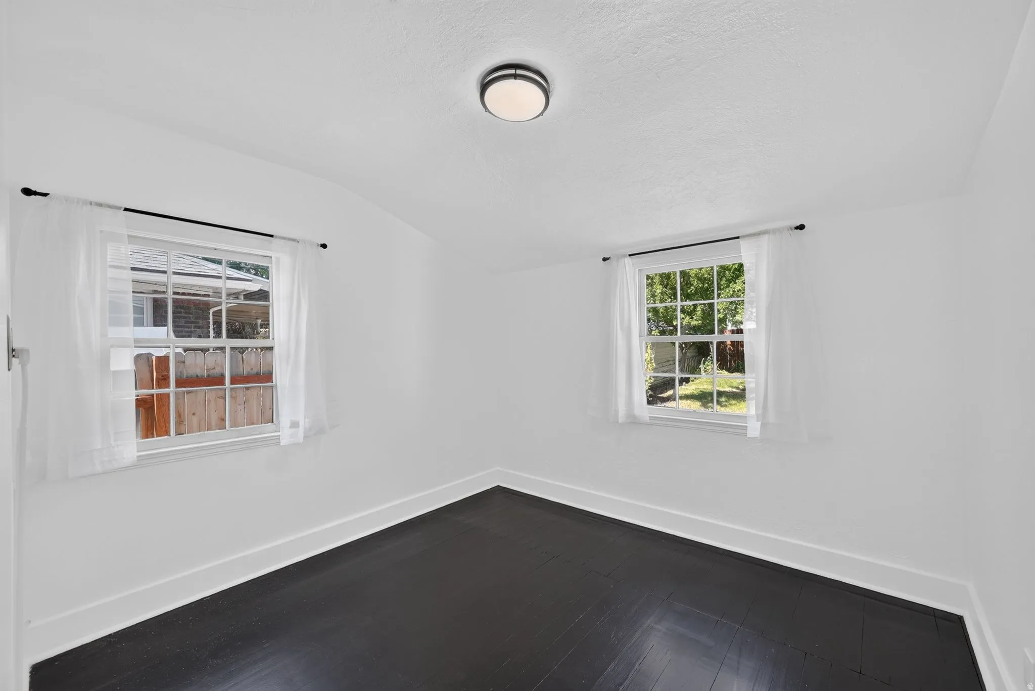 Two double-hung windows with white trim, dark wood-finish flooring, white walls, and a ceiling-mounted light fixture
