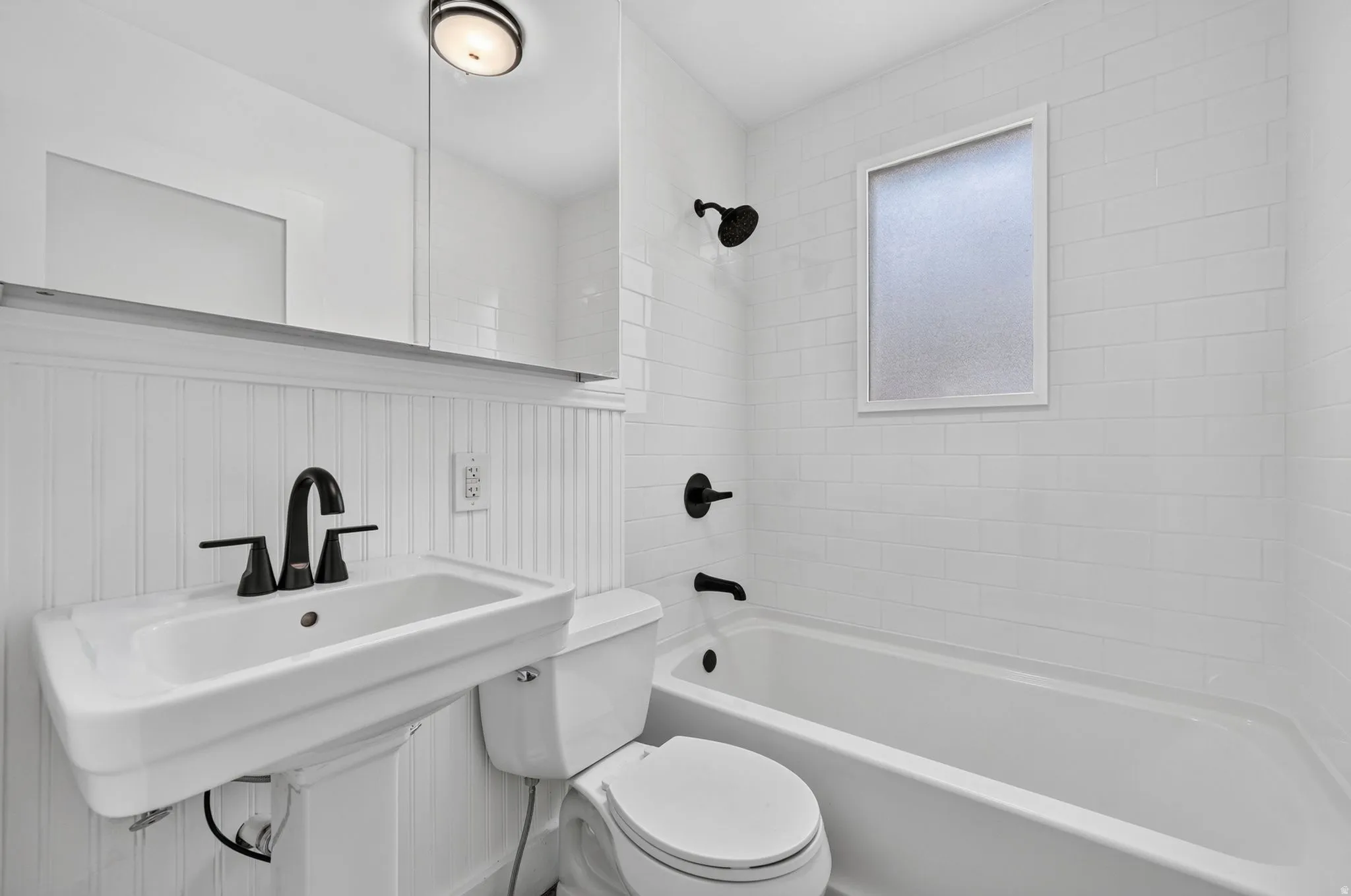 Pedestal sink with matte black faucet, subway tile shower surround, shower/tub combination, and frosted window