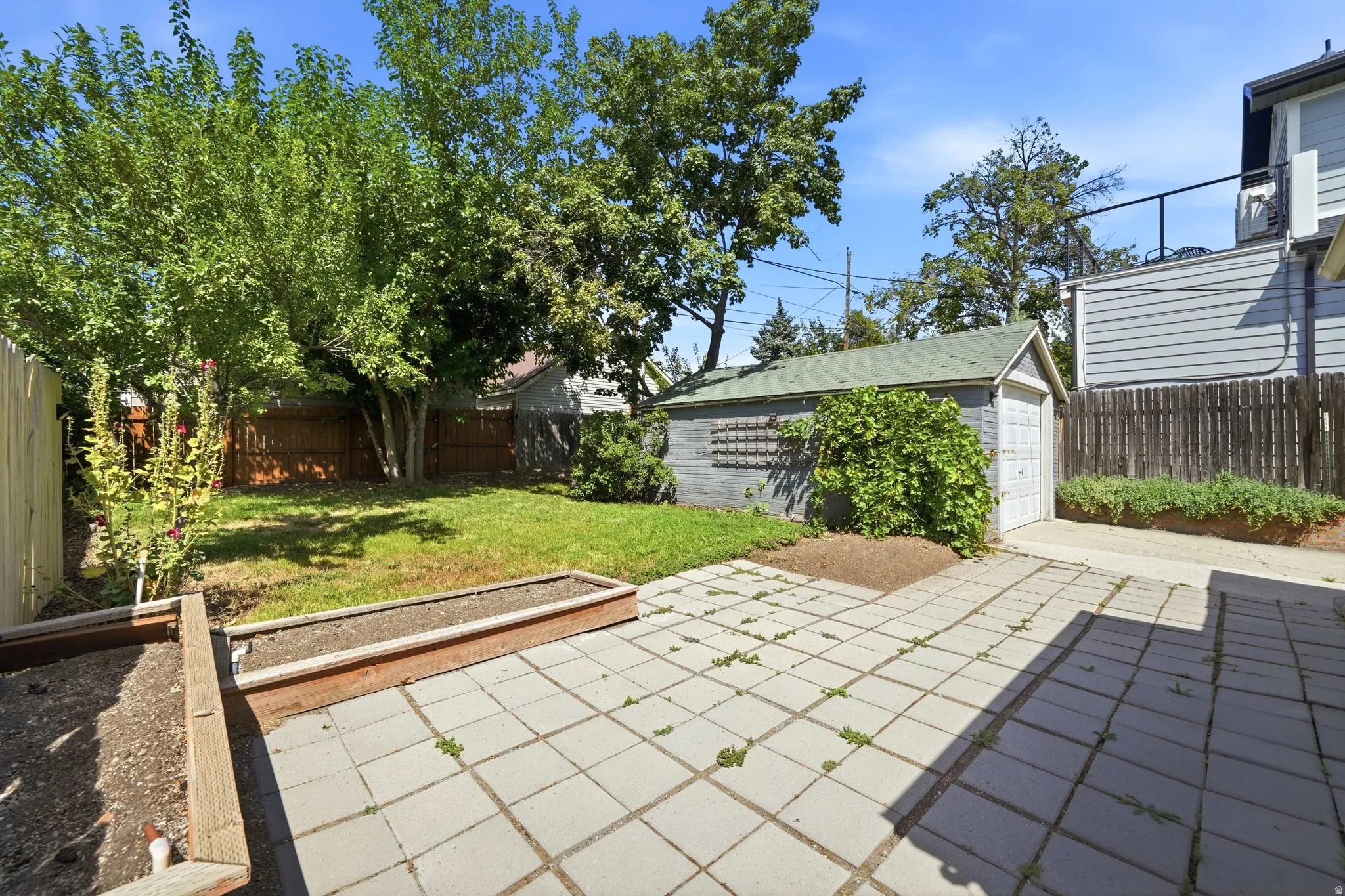 Paved patio area, raised planter beds, grassy expanse, mature trees, and detached garage
